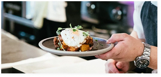 The head chef is holding a plate with a cooked dish, garnished with a fried egg and herbs