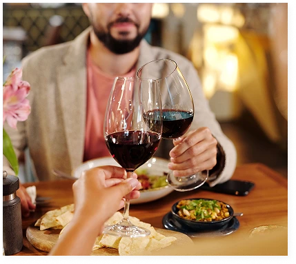 A couple are clinking glasses of red wine at a restaurant table laden with appetisers
