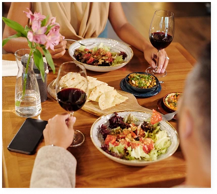 A man and a woman are having lunch in a restaurant, enjoying fresh salads, starters and glasses of red wine