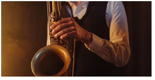 A musician in a white shirt and waistcoat is playing the saxophone