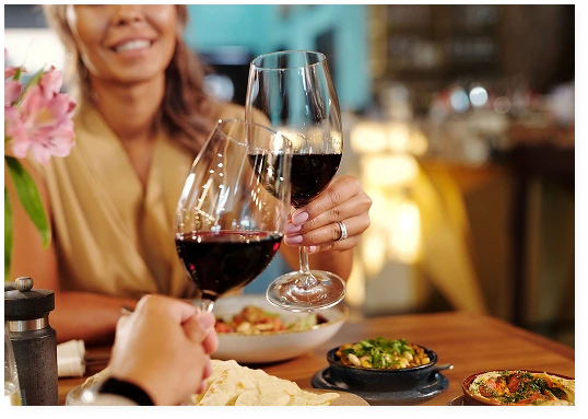 A couple clink their glasses of red wine whilst having dinner at a restaurant
