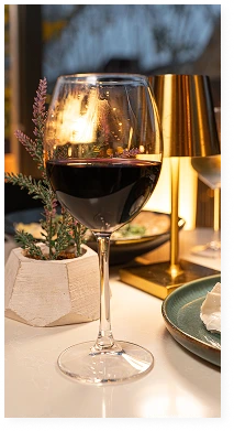 A glass of red wine on the table next to a table lamp and a small potted plant