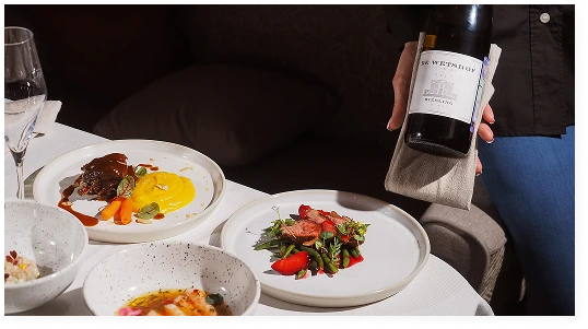 A waiter is holding a bottle of wine next to a table laden with exquisite restaurant dishes