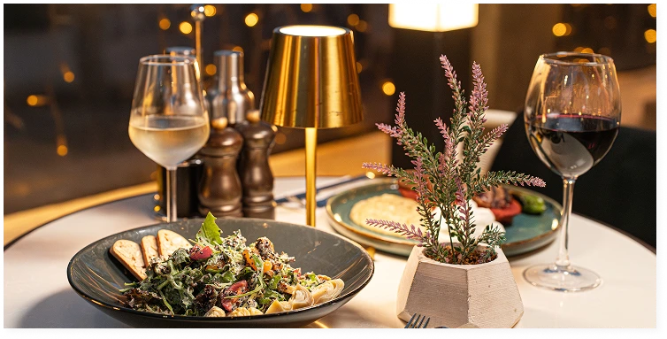 An elegant restaurant table set with gourmet dishes, white and red wine, and warm ambient lighting. The image conveys a refined dining atmosphere with intimate evening ambiance.